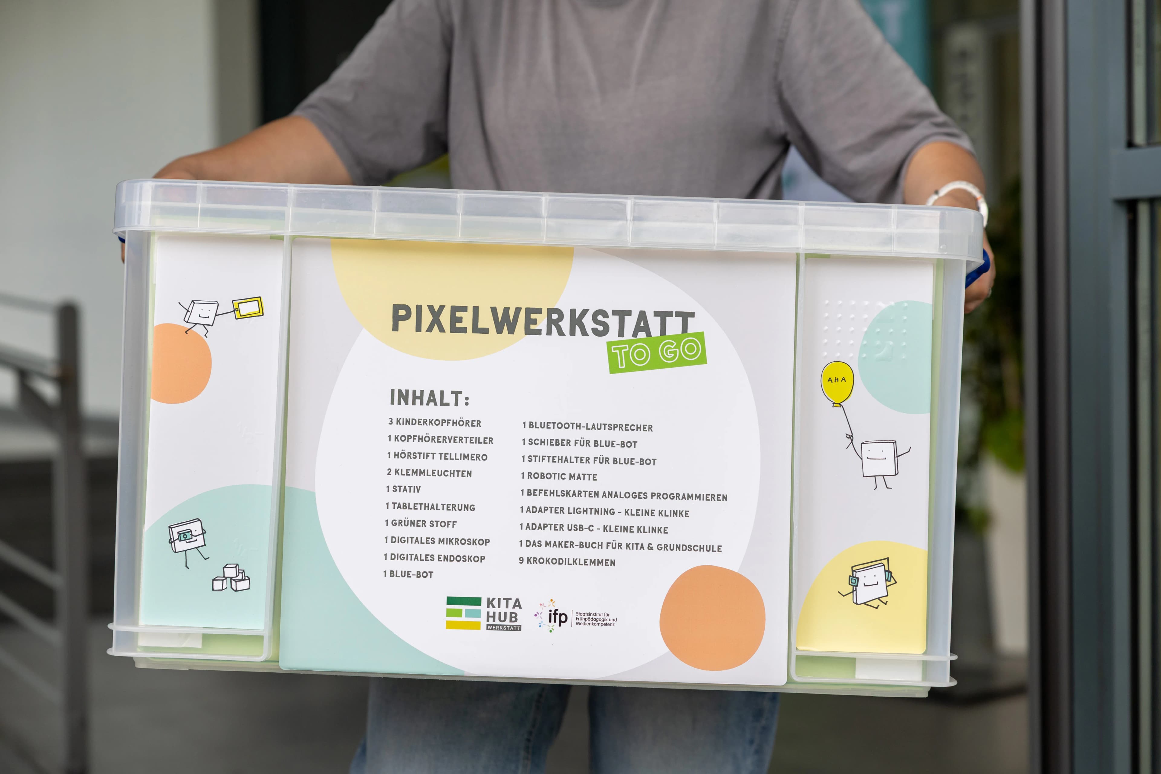Die Leihbox der PIXELWERKSTATT to go: eine durchsichtige Box mit blauen Griffen und buntem Aufkleber
